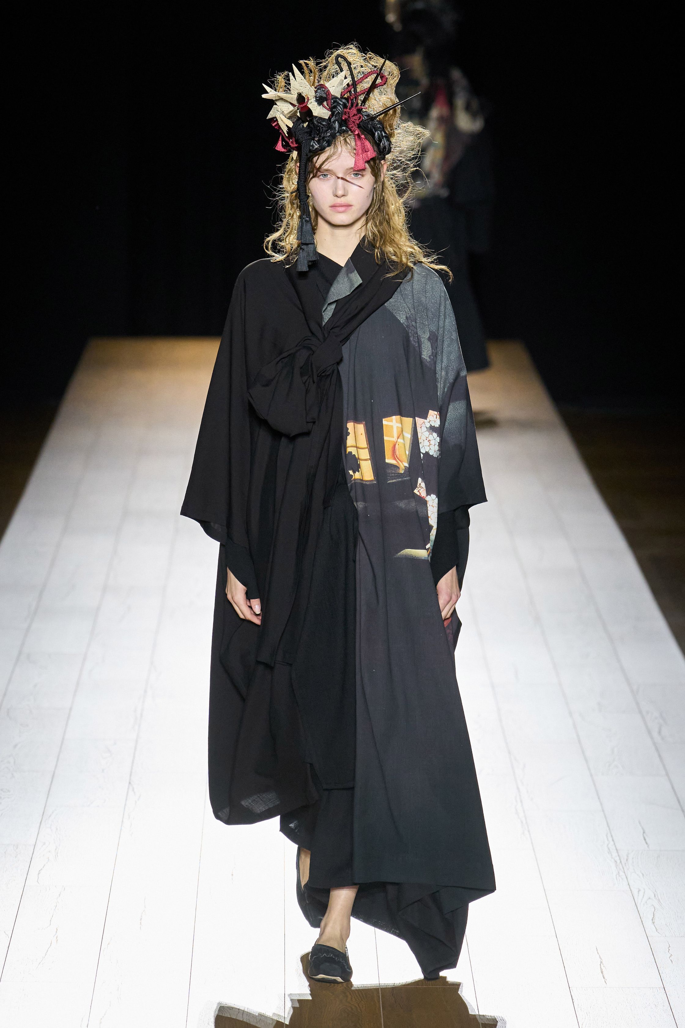 Yohji Yamamoto 本季依然延续标志性的黑色哲学：宽松层叠轮廓、和服式结构与手工拼接面料形成一种诗意而深沉的东方美学。夸张头饰与飘逸衣摆让整场秀像一场黑色戏剧，既神秘又极具艺术感-顽石频道趋势研究
